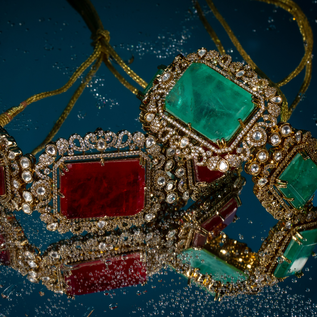 Two ornate Indian chokers in emerald green and deep red, featuring gold-plated settings with crystal embellishments