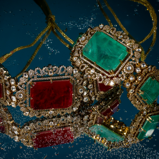 Two ornate Indian chokers in emerald green and deep red, featuring gold-plated settings with crystal embellishments