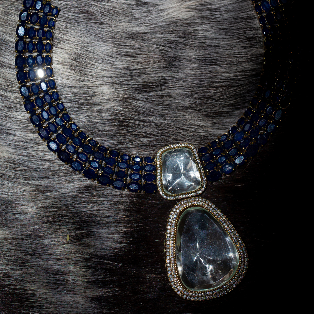 The Reign Necklace Set in gold plated brass with glass polki pendants and sapphire blue crystal accents, includes matching earrings.

