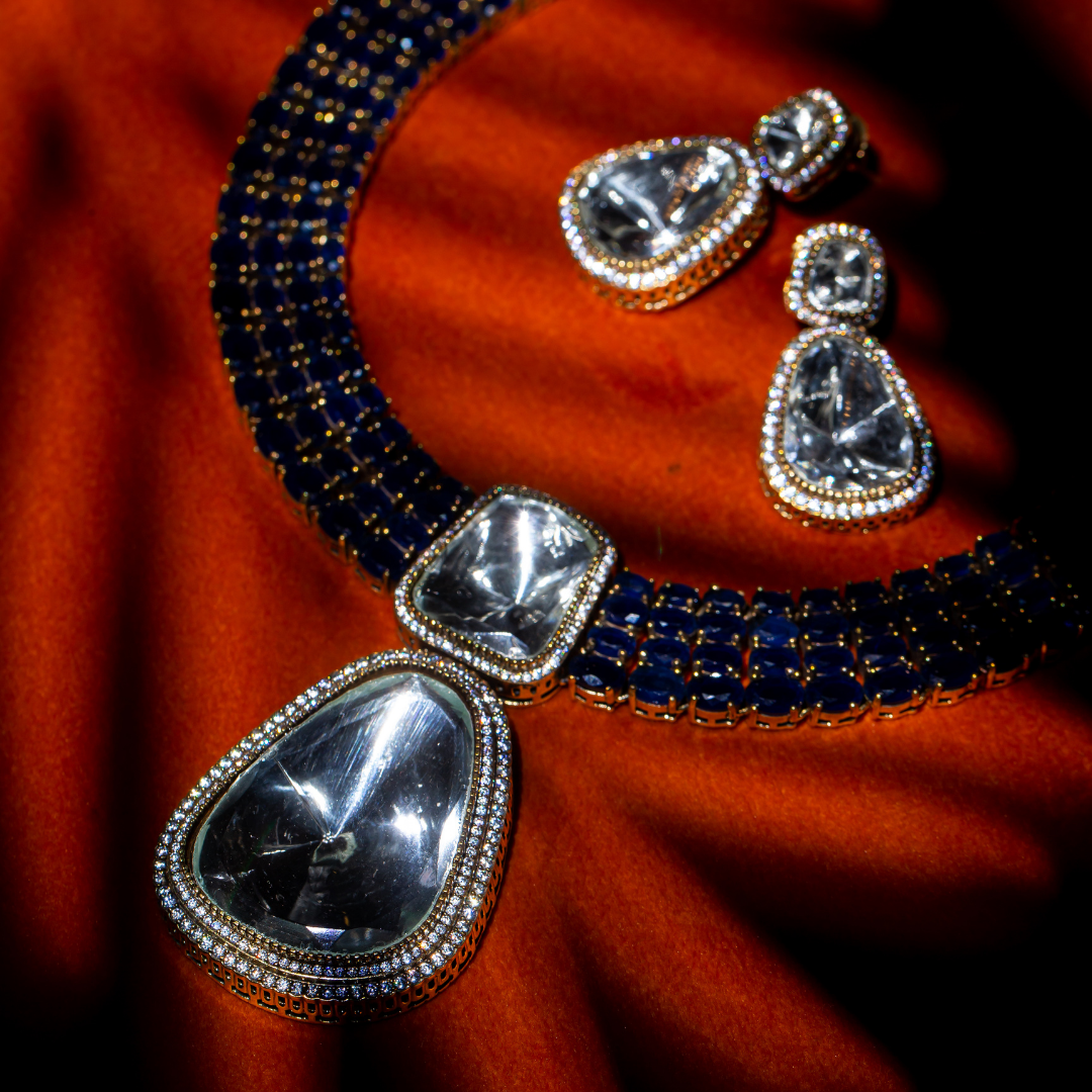 The Reign Necklace Set in gold plated brass with glass polki pendants and sapphire blue crystal accents, includes matching earrings.

